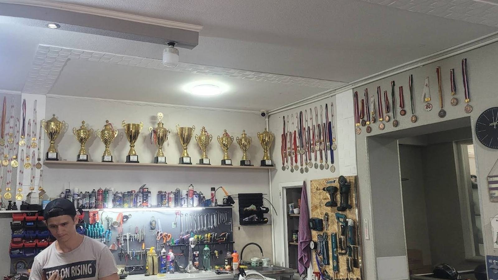 Mechanic at the workbench under a shelf of racing trophies
